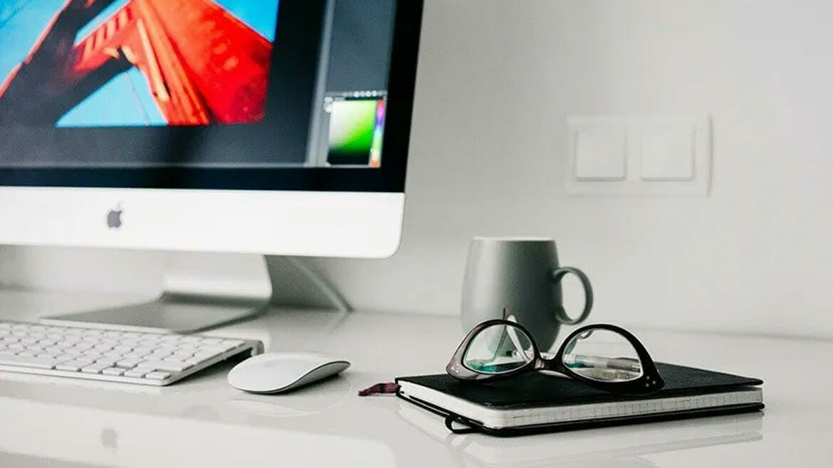 Clean Work Area: Organized Desk with MacBook Pro, Mug, Notebook, and Glasses