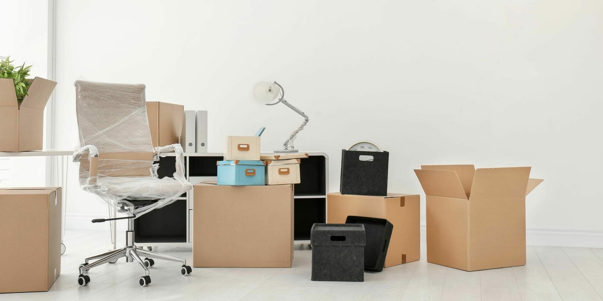 Office with boxes and a chair wrapped in transparent plastic, indicating a move-out process.