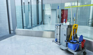 Modern office corridor with glass windows and a cleaning cart stocked with products.