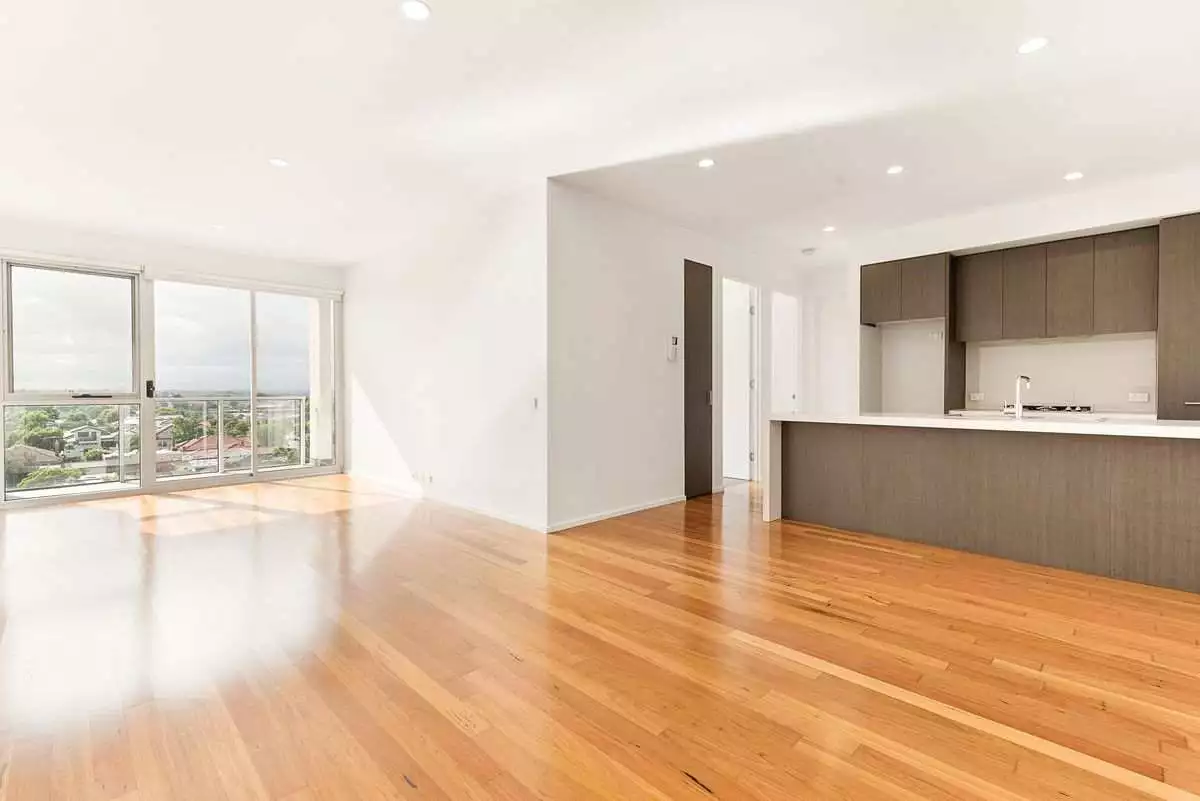 An unoccupied apartment featuring gleaming wooden floors and a modern, clean kitchen.