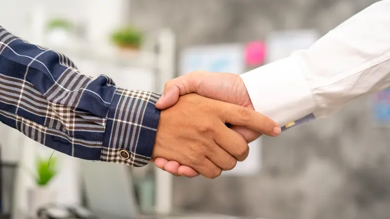 Close-up of two people shaking hands, one wearing a plaid shirt and the other wearing a white dress shirt.